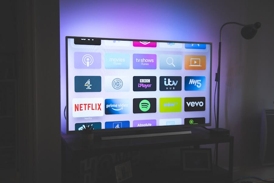 Smart TV in a dim living room displaying a grid of streaming app icons (e.g., Netflix, Prime Video, Spotify, BBC iPlayer) with a purple backlight and a floor lamp beside it.