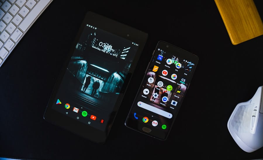 An Android tablet and smartphone on a dark desk, screens on—tablet with a moody city staircase wallpaper and phone showing app icons—beside a white keyboard and ergonomic mouse.
