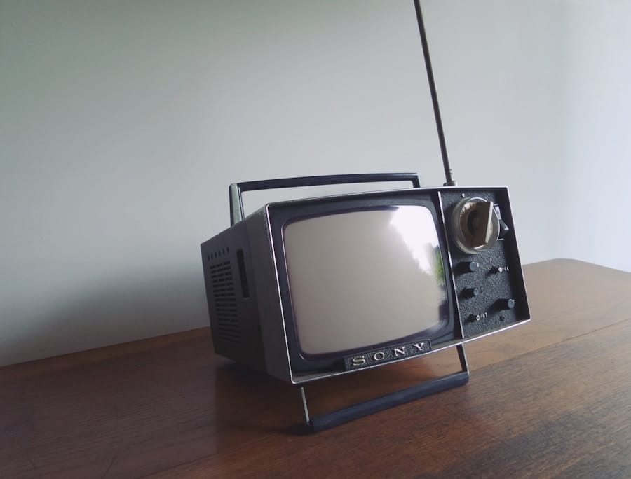 Retro Sony portable CRT television with a telescopic antenna, side knobs, and carry handle, sitting on a wooden table against a plain wall.