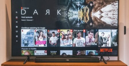 A flat‑screen TV on a wooden media console displays the Netflix home screen with the series Dark highlighted, rows like Continue Watching and Popular on Netflix visible, and a soundbar beneath the screen.