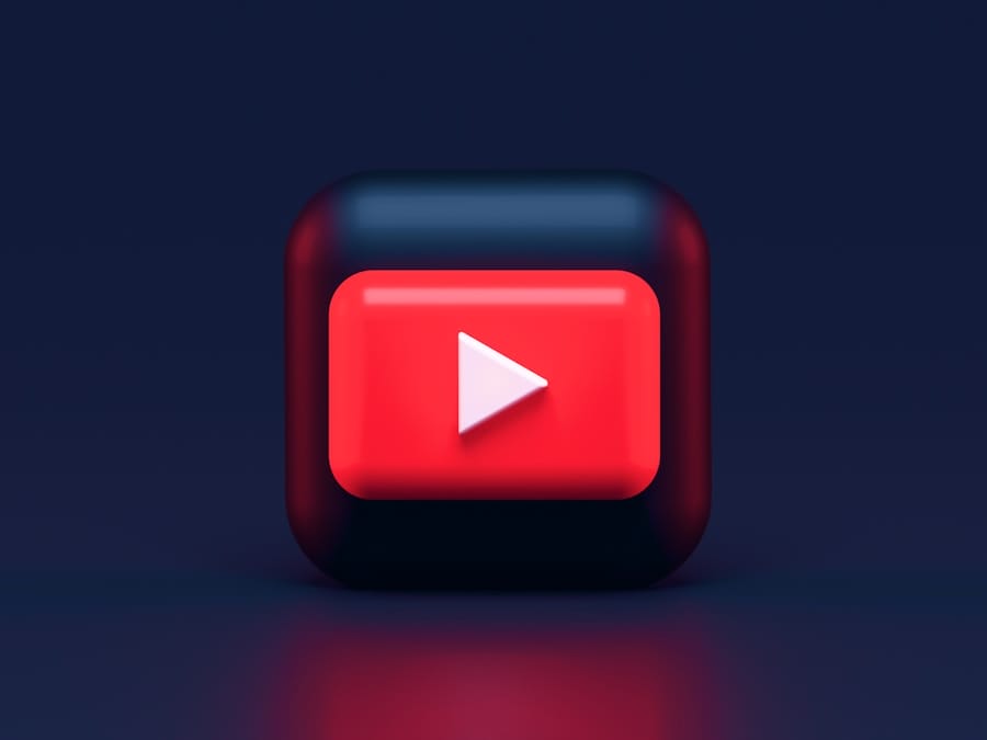 3D red play button with a white triangle on a rounded dark square, resembling the YouTube logo, against a dark gradient background.