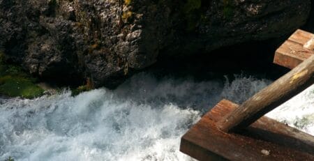 Whitewater rushes through a narrow rocky gorge beneath a moss-covered cliff, viewed from a wooden platform in the foreground.