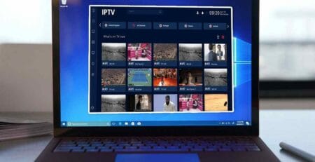 Laptop on a desk running Windows 10 with an IPTV app open, showing a dark blue dashboard and a grid of live TV channel thumbnails.