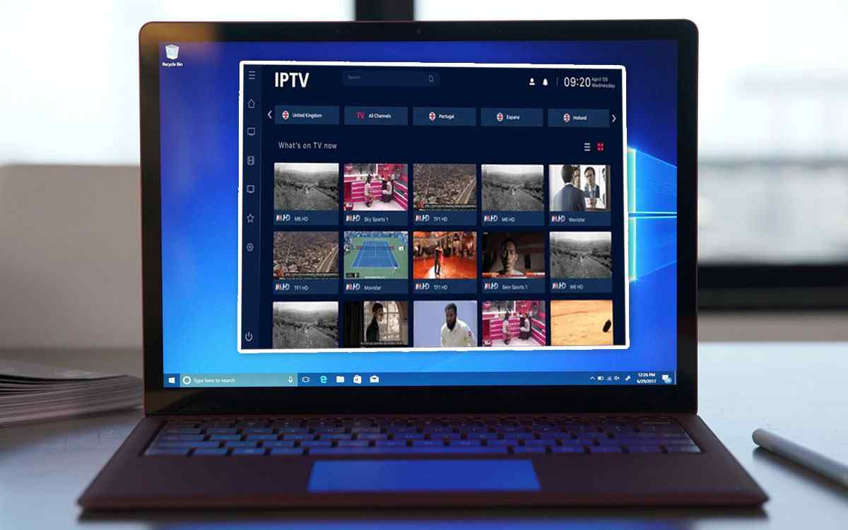 Laptop on a desk running Windows 10 with an IPTV app open, showing a dark blue dashboard and a grid of live TV channel thumbnails.